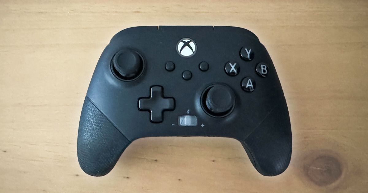 A black Xbox-style controller sat on top of a light brown wooden surface.